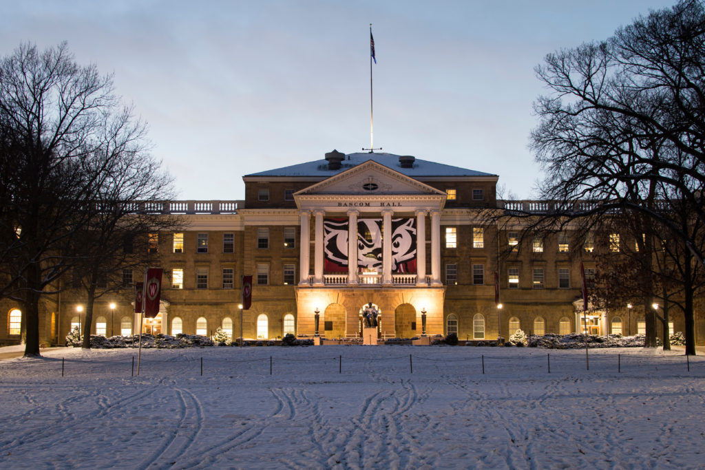 Dusk falls to nighttime as a newly designed banner with a graphic of mascot Bucky Badger's face hangs between the columns of Bascom Hall at the University of Wisconsin-Madison during winter on Nov. 25, 2014. In the foreground, several W Crest banners fly on snow-covered Bascom Hill. (Photo by Jeff Miller/UW-Madison)